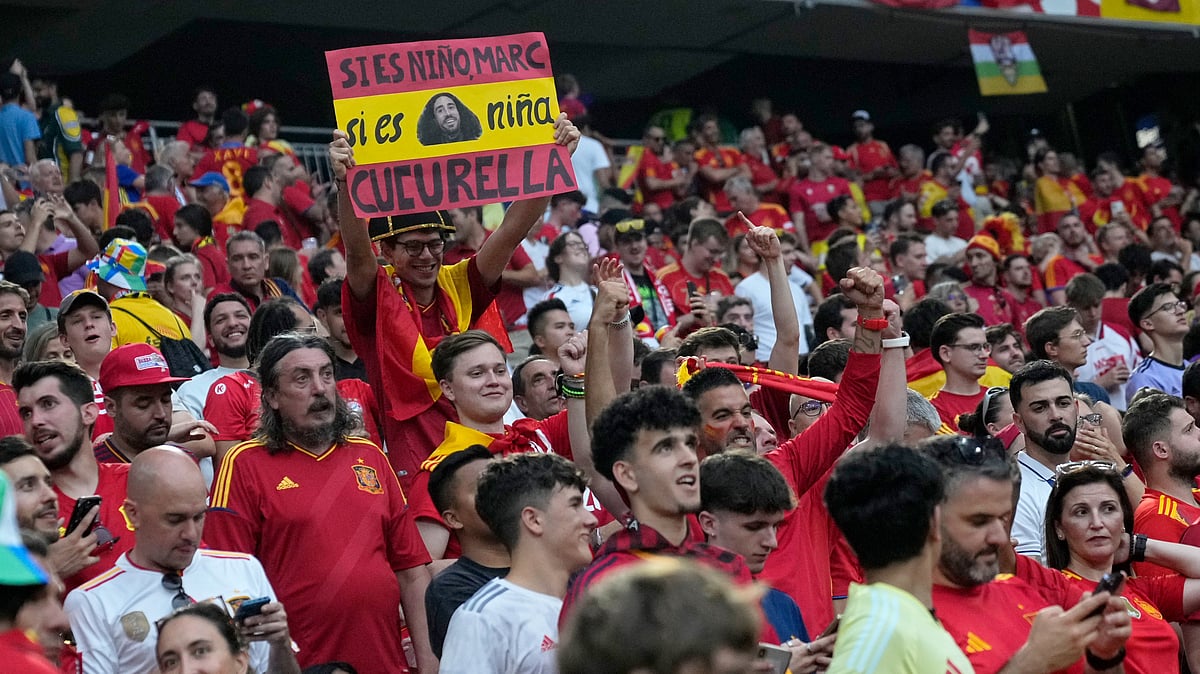 (AP Photo/Matthias Schrader) : A Spain supporter on the stands holds up a poster with a picture of Spain's Marc Cucurella while waiting for the start of a semifinal match between Spain and France at the Euro 2024 soccer tournament in Munich, Germany, Tuesday, July 9, 2024. Words in Spanish read, If it's a boy, Marc, if it's a girl, Cucurella. 
